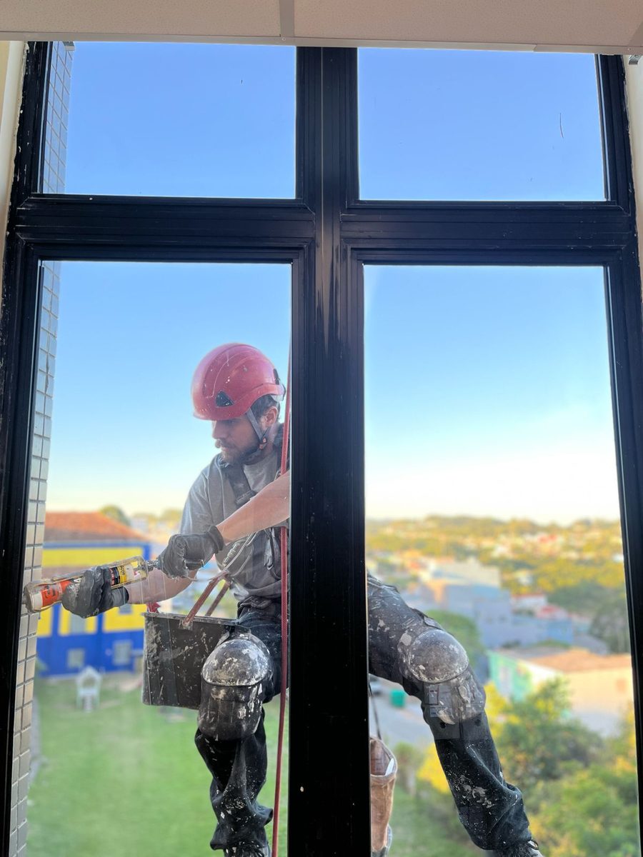 Profissional aplicando vedação em esquadria durante manutenção predial